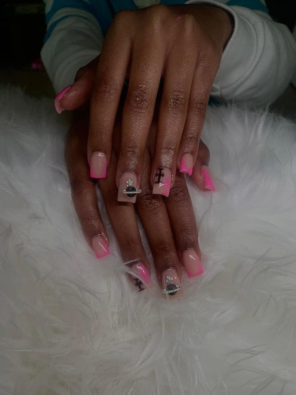 Pink french-tip nails with charms on a white fur background